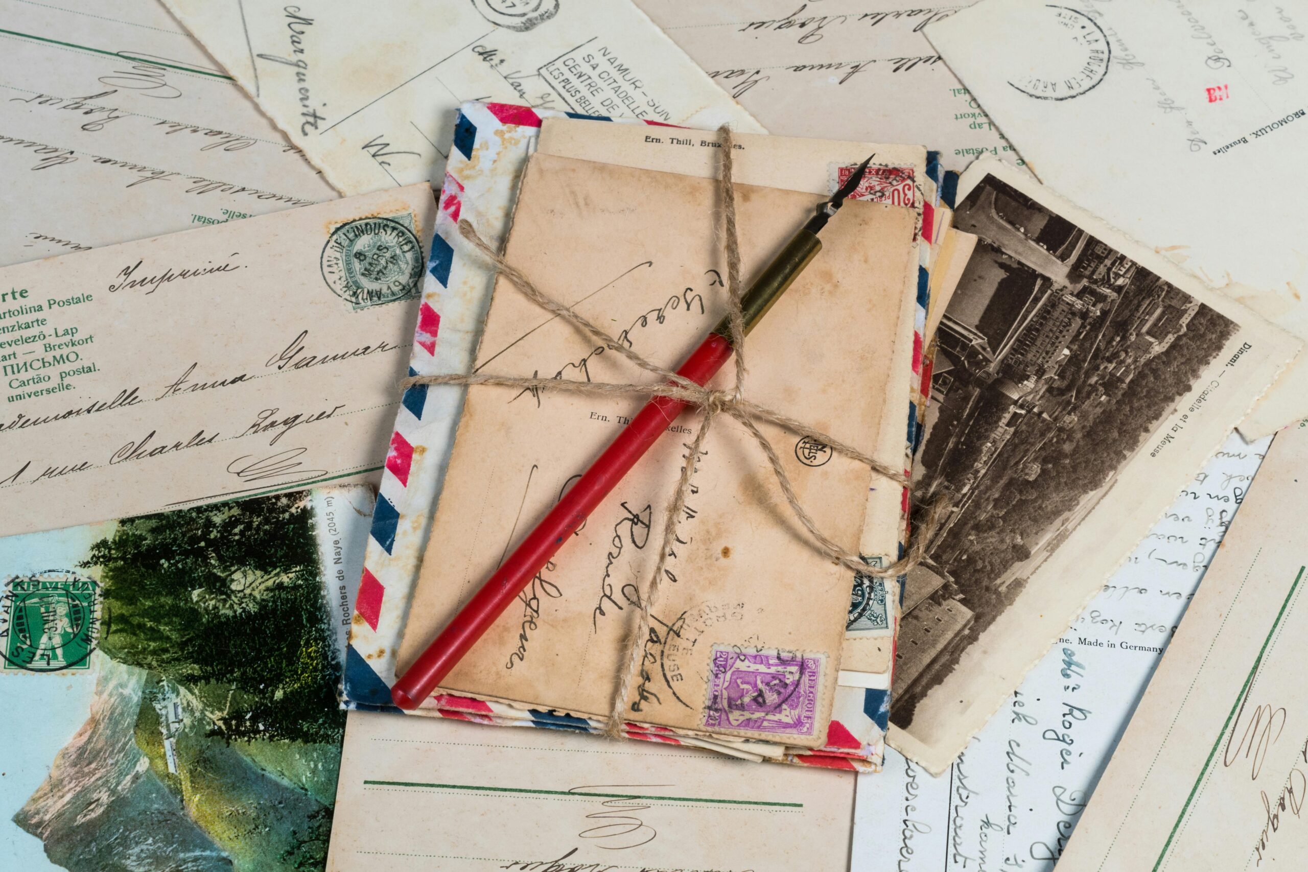 A collection of vintage postcards and envelopes tied with twine, featuring a pen and old stamps.