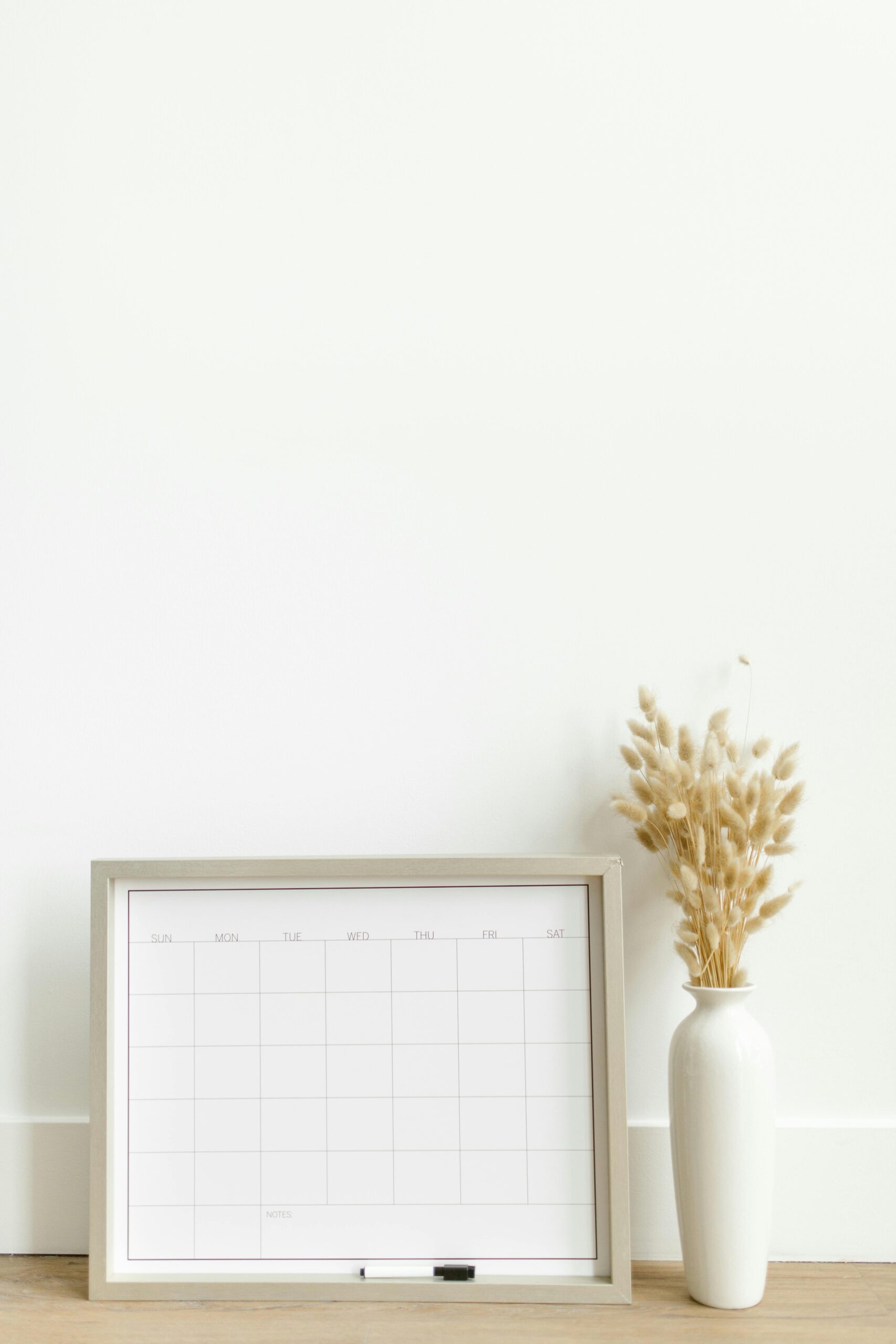 A minimalist setup featuring a framed calendar and decorative vase against a white background.